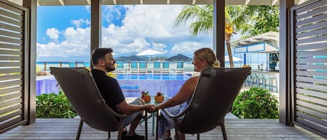 Two people seated at a table on a wooden deck with a view of a pool and mountains in the background.