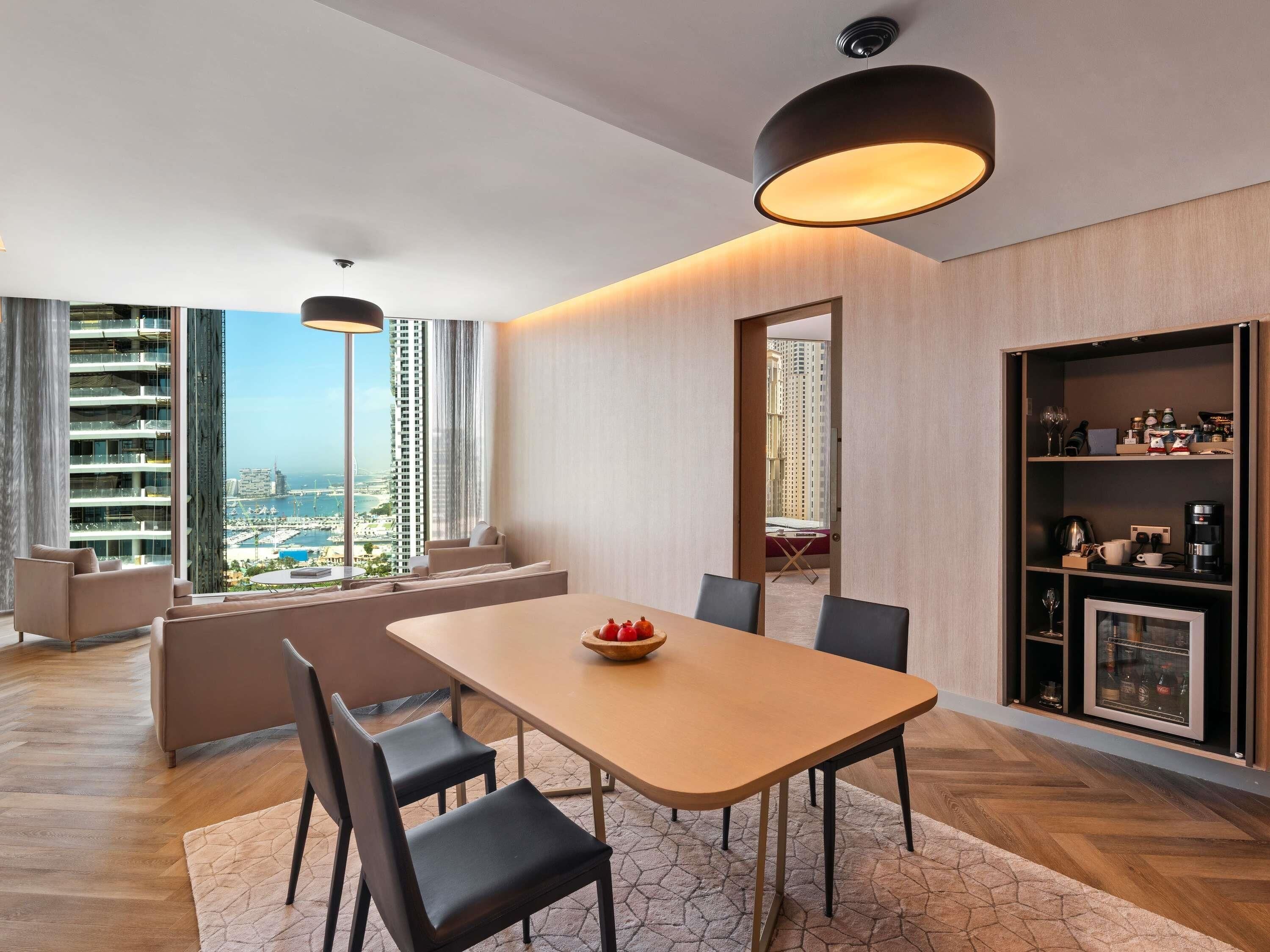 Un espace de salle à manger moderne avec une table en bois, des chaises noires et une vue sur le paysage urbain, visible à travers de grandes fenêtres.