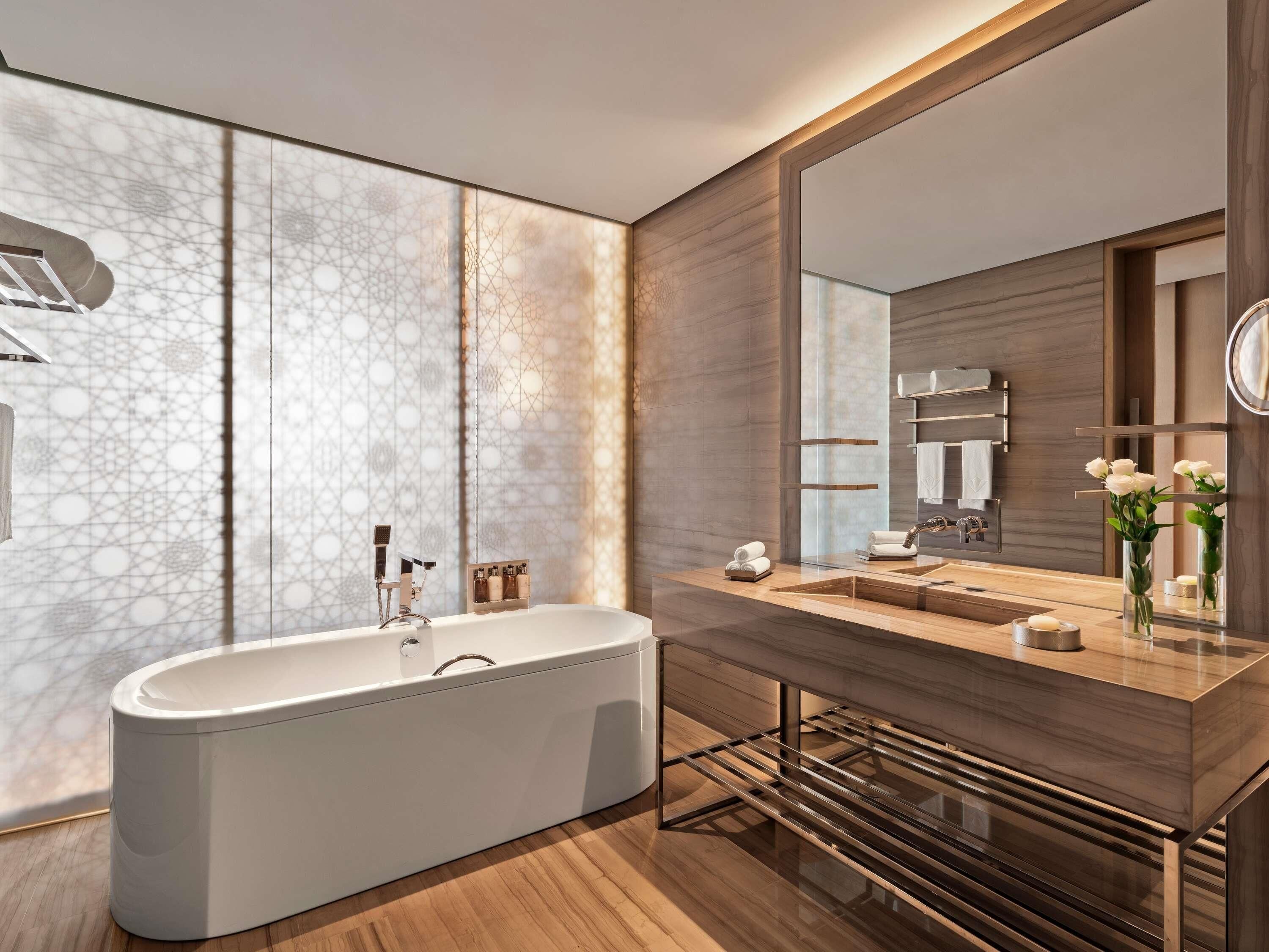A modern bathroom with a freestanding bathtub, a large mirror, and a wooden vanity with a sink and towel rack.