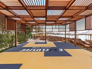 A covered outdoor seating area with lounge chairs and umbrellas, a wooden pergola structure, and a view of the water.
