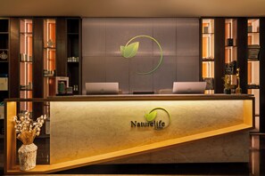 A reception desk with a Naturelife logo, two laptops, and a decorative vase with dried plants.