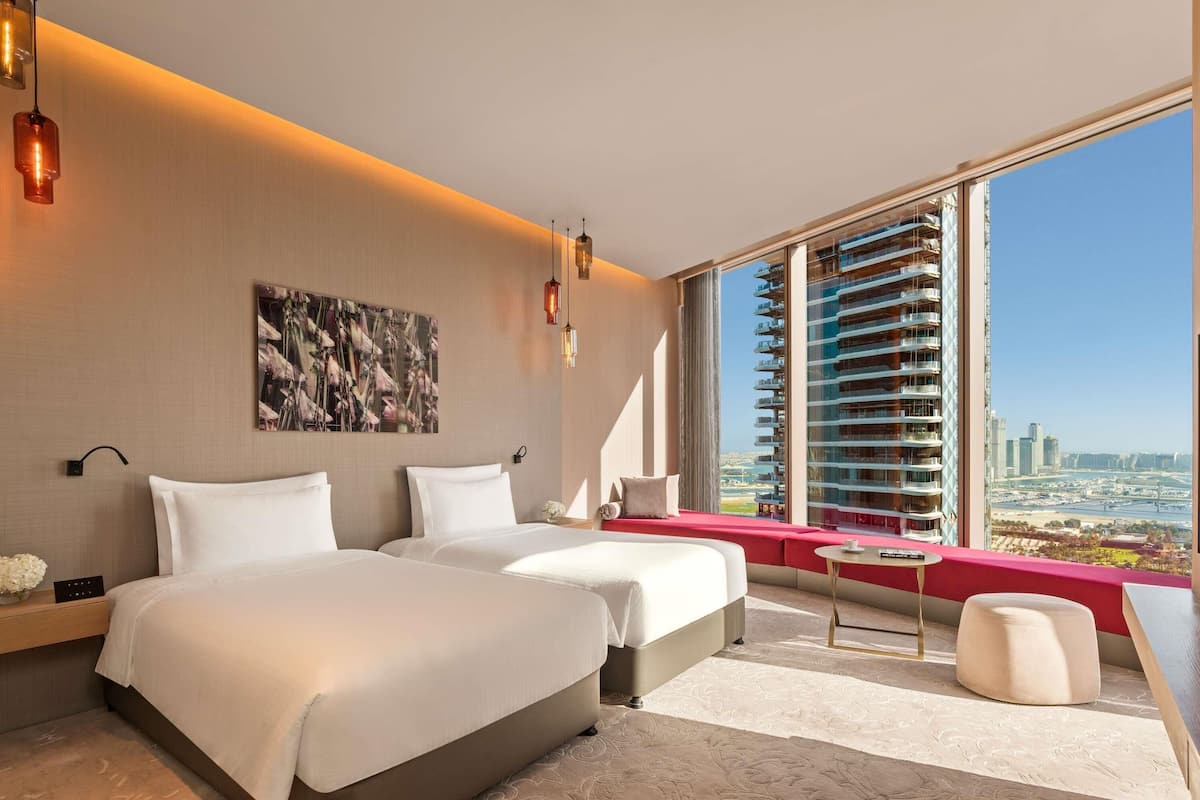 A modern hotel room with two beds, a large window with a city view, and a red accent wall.