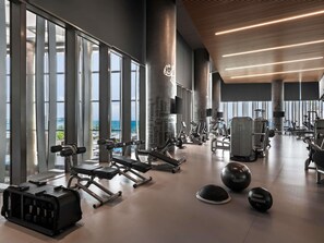 A modern gym with various exercise equipment, large windows, and a view of the ocean.