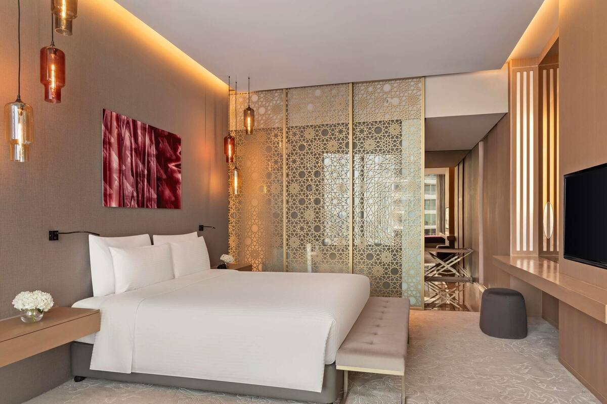 A modern hotel room with a large bed, bedside tables, a TV, and a decorative wall panel.