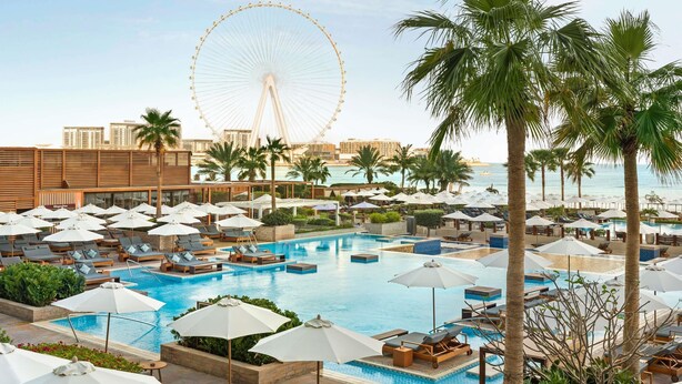 A resort with multiple swimming pools, lounge areas, palm trees, and a Ferris wheel in the background. - Rixos Premium Dubai JBR (Dubai)