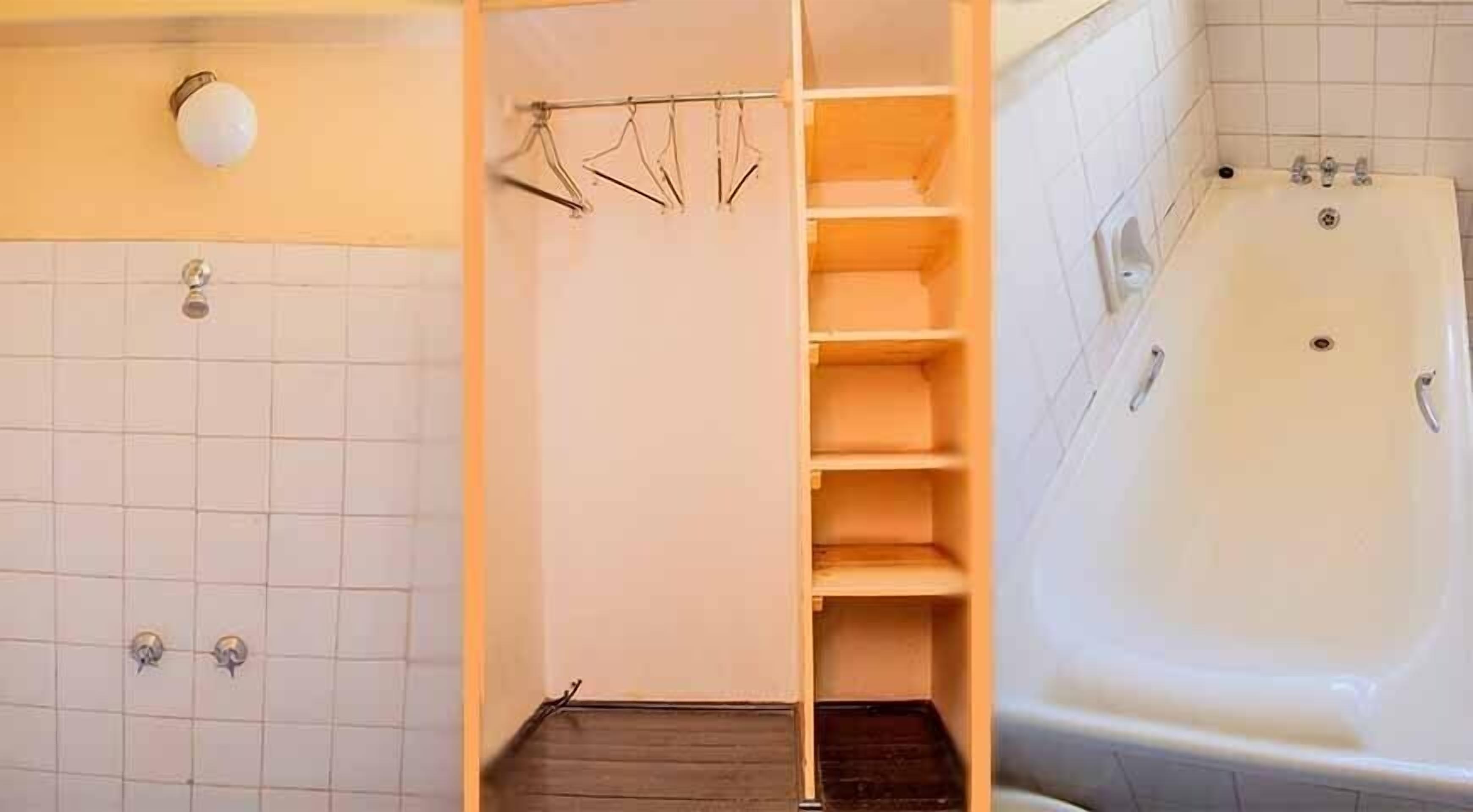 A bathroom with a bathtub, a shower area, and a wooden shelf unit.