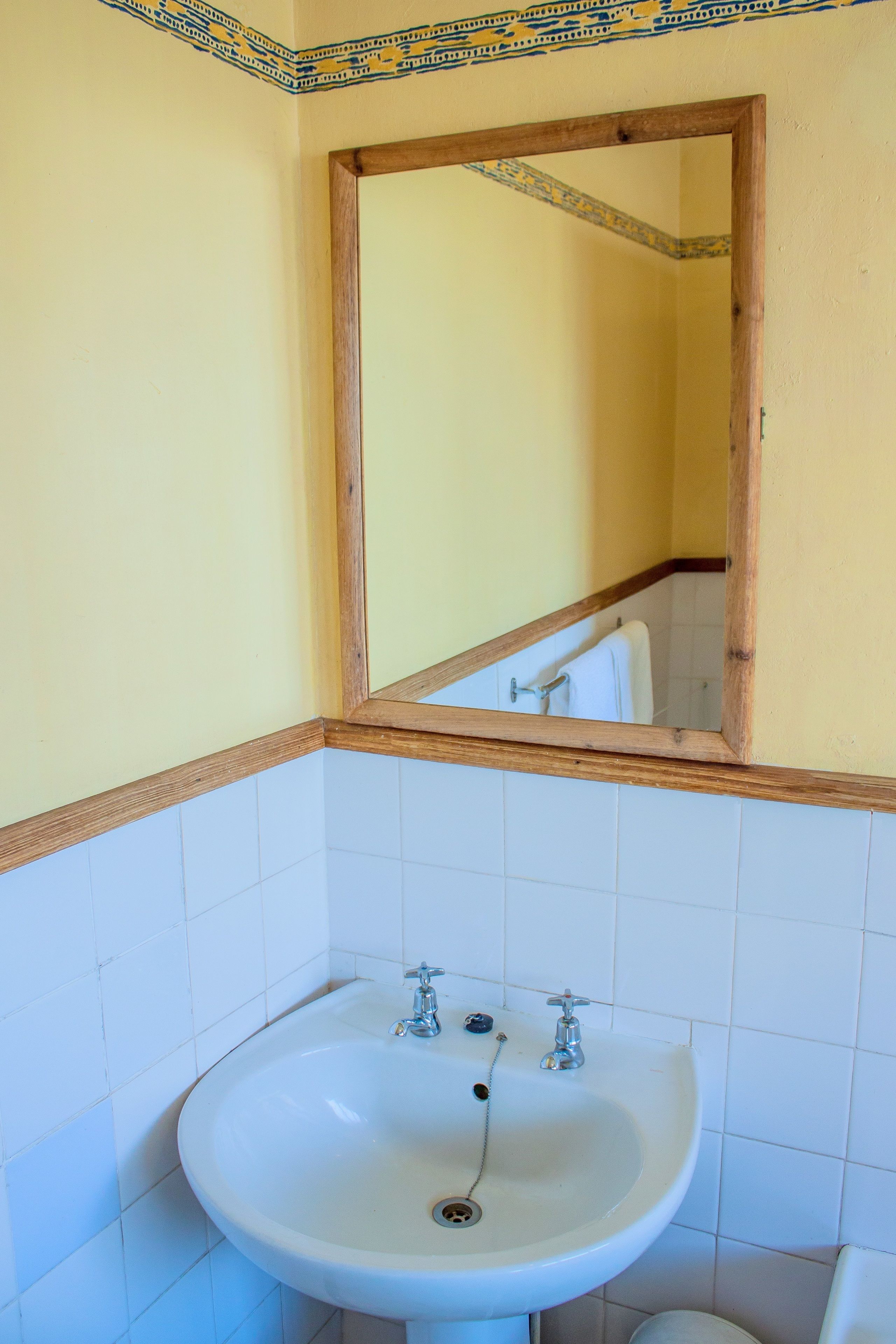 A bathroom with a white sink, wooden frame around the mirror, and yellow walls.