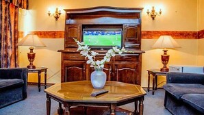 A hotel room with a wooden cabinet, a television, two lamps, and a vase with flowers on a table. - The Grey's Inn (Bulawayo)