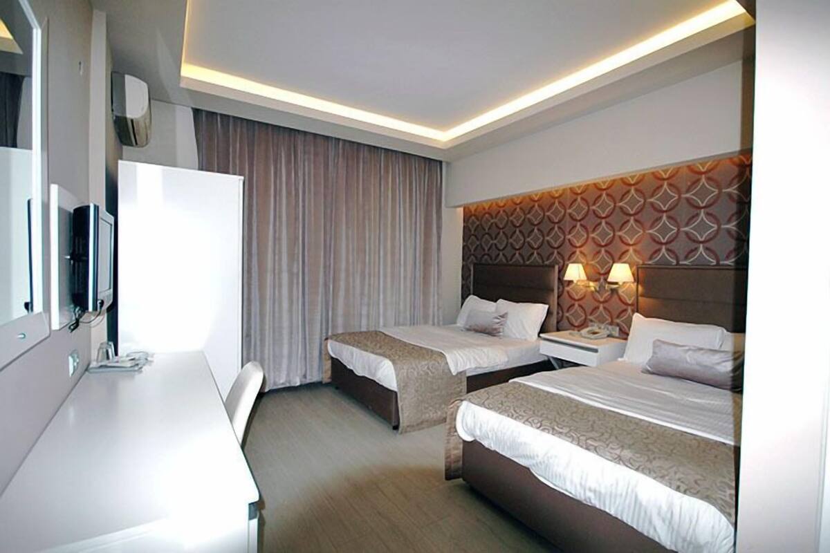 A hotel room with two beds, a desk, a TV, and a patterned headboard.