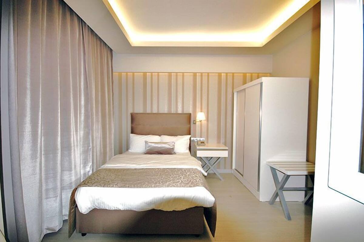 A hotel room with a large bed, a bedside table with a lamp, a wardrobe, and a small table.