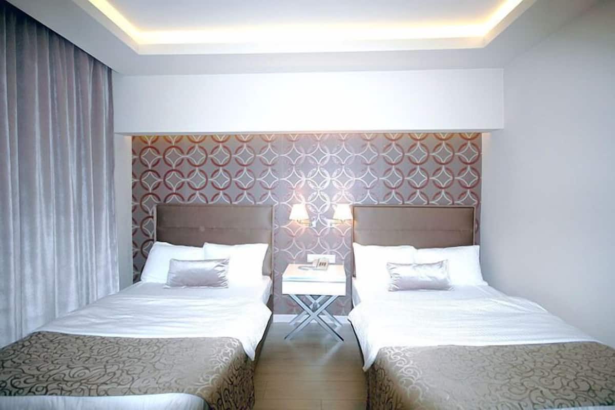A hotel room with two beds, a small table, and a patterned headboard.