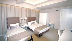 A hotel room with two beds, a desk, a chair, a wardrobe, and a small table. - Kent Otel (Samsun)