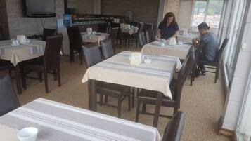 A restaurant with multiple tables, chairs, and a television mounted on the wall.