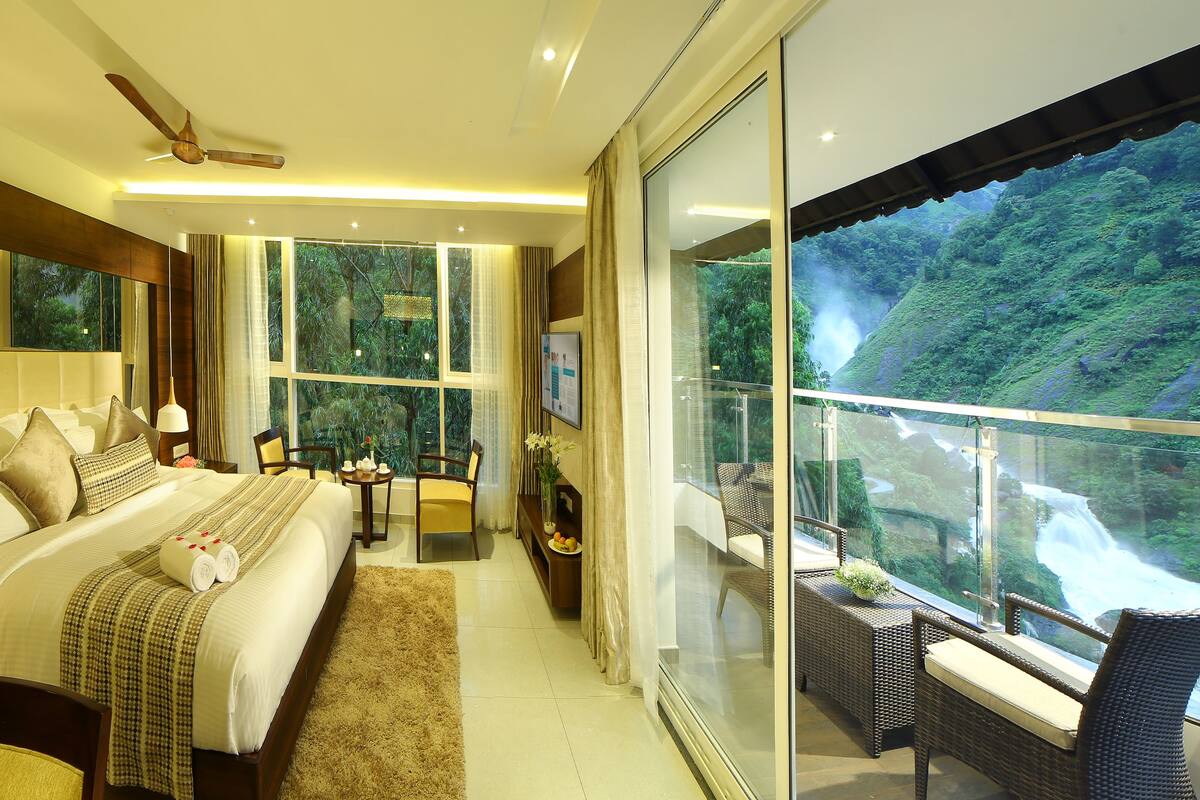 A hotel room with a large bed, a balcony with a view of a waterfall, and a television on the wall.