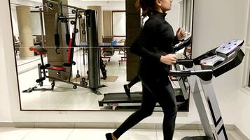A woman running on a treadmill in a gym with exercise equipment and a large mirror on the wall.