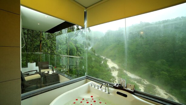 Un baño moderno con una bañera grande, un rincón con asientos protegidos por vidrio y vistas a un valle boscoso.