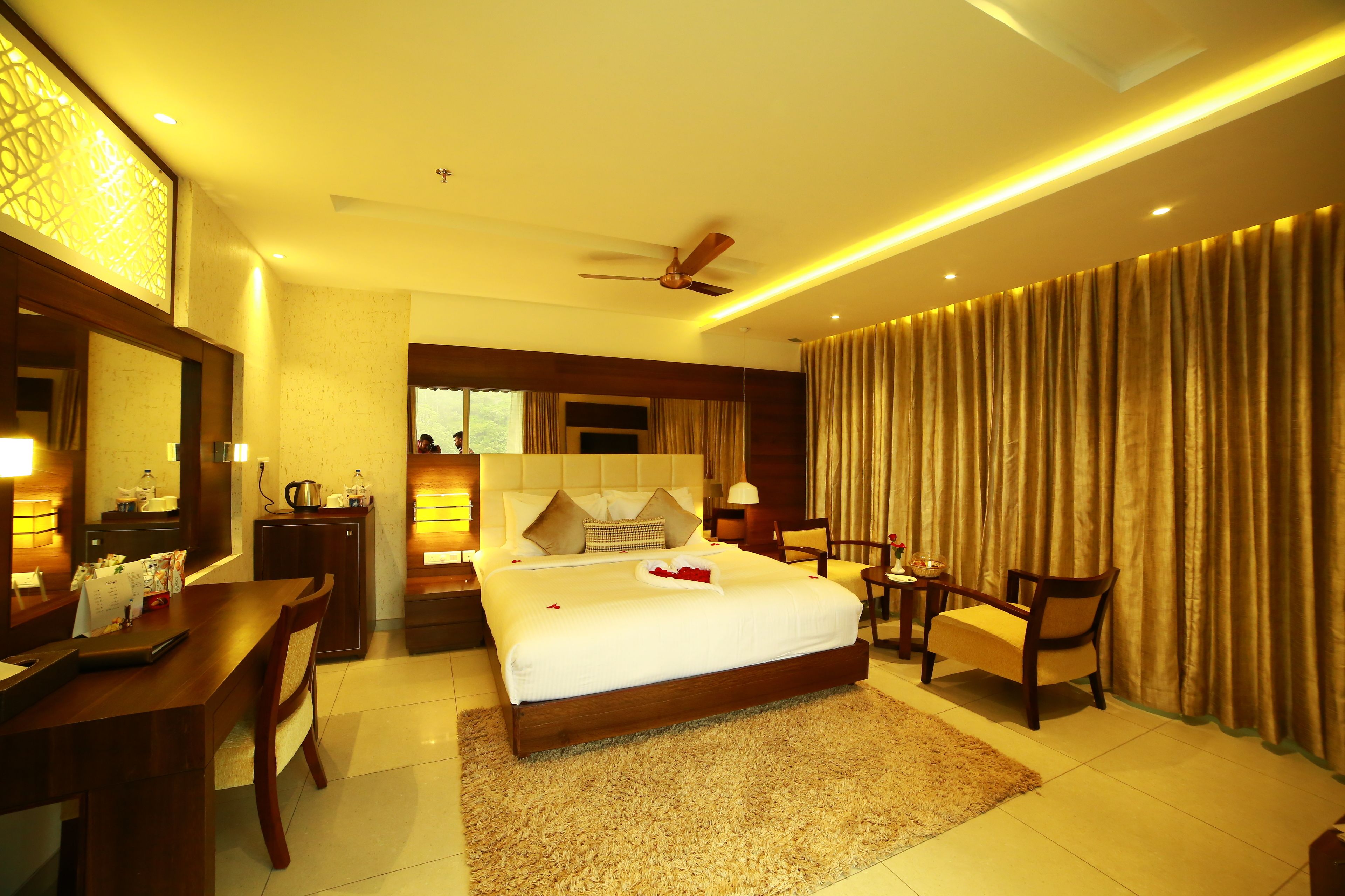 A spacious hotel room with a large bed, a desk, a chair, and a vanity with a mirror.