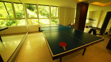 Una mesa de ping pong con una paleta roja en una habitación con ventanas grandes y una cinta de correr.