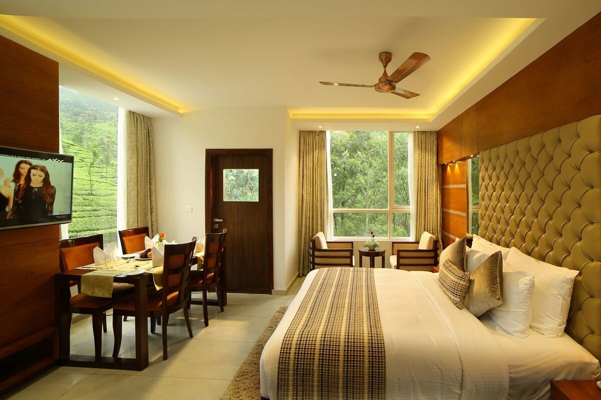 A hotel room with a bed, a desk, chairs, a television, and a large window.