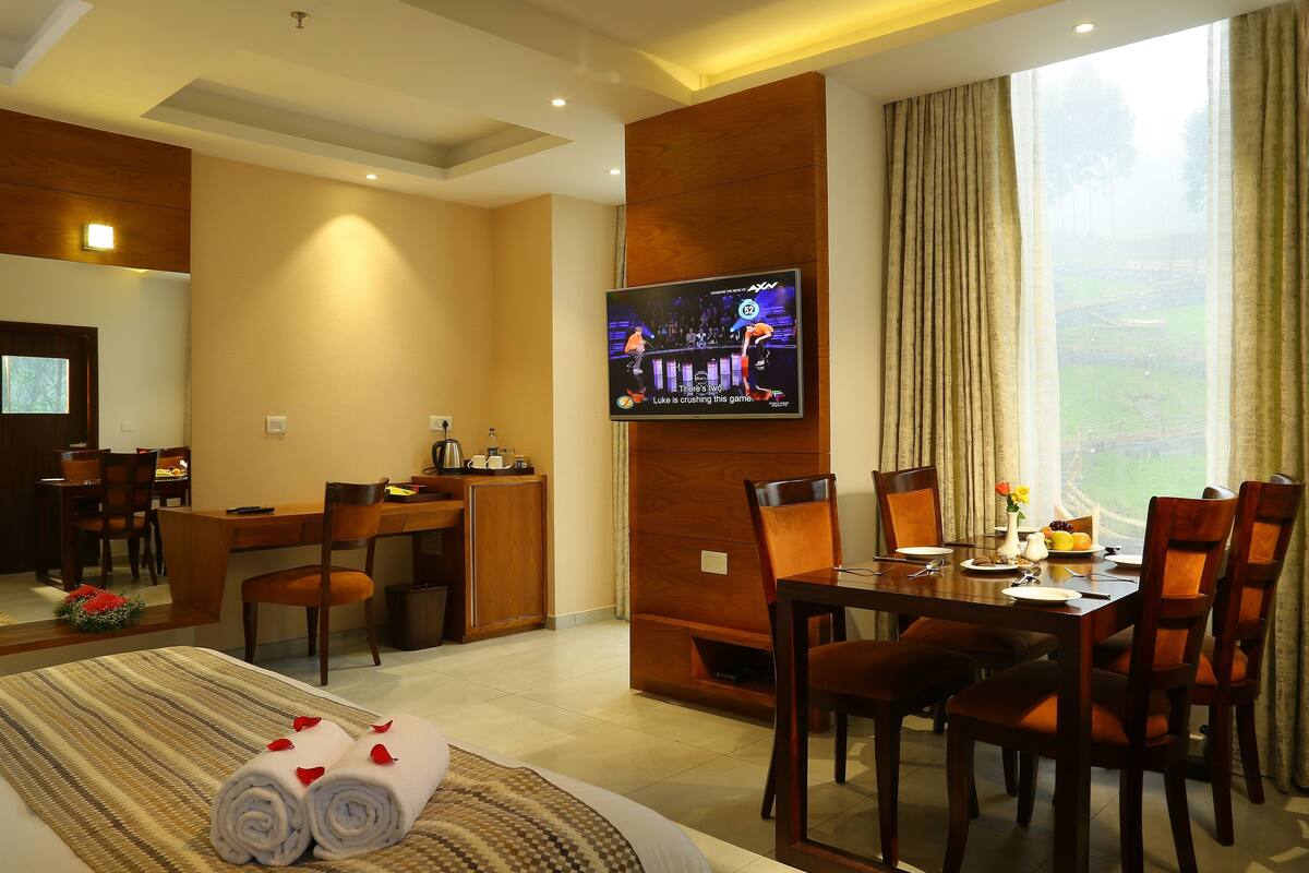 A hotel room with a bed, a desk, a TV, and a dining area.