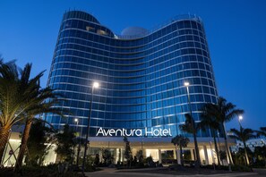 A modern hotel with a curved facade, palm trees, and a clear sky. - Universal's Aventura Hotel (Orlando)