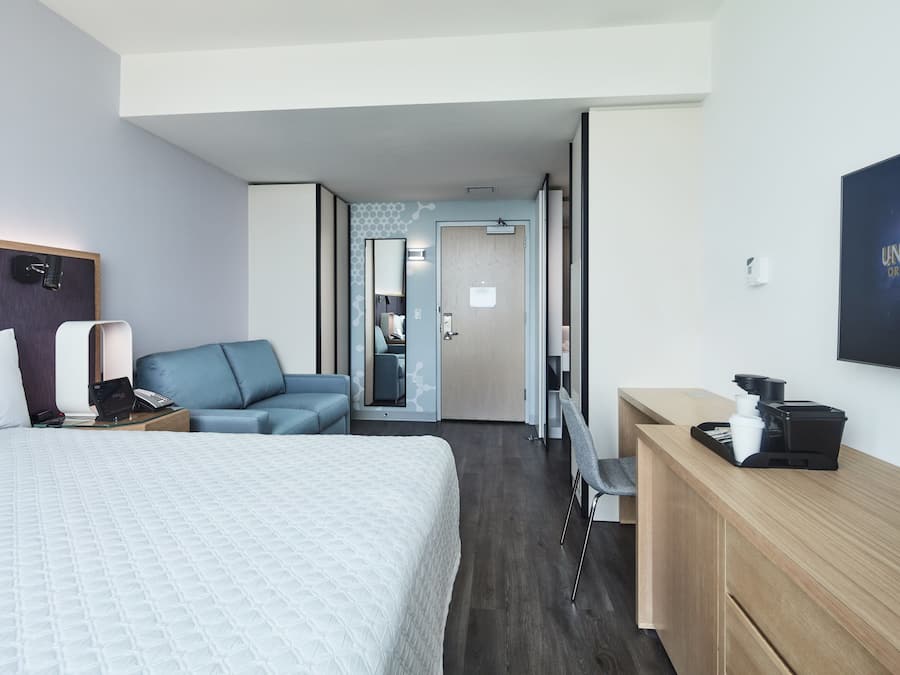 Habitación de hotel con cama, escritorio con cafetera, zona de estar y televisor montado en la pared.