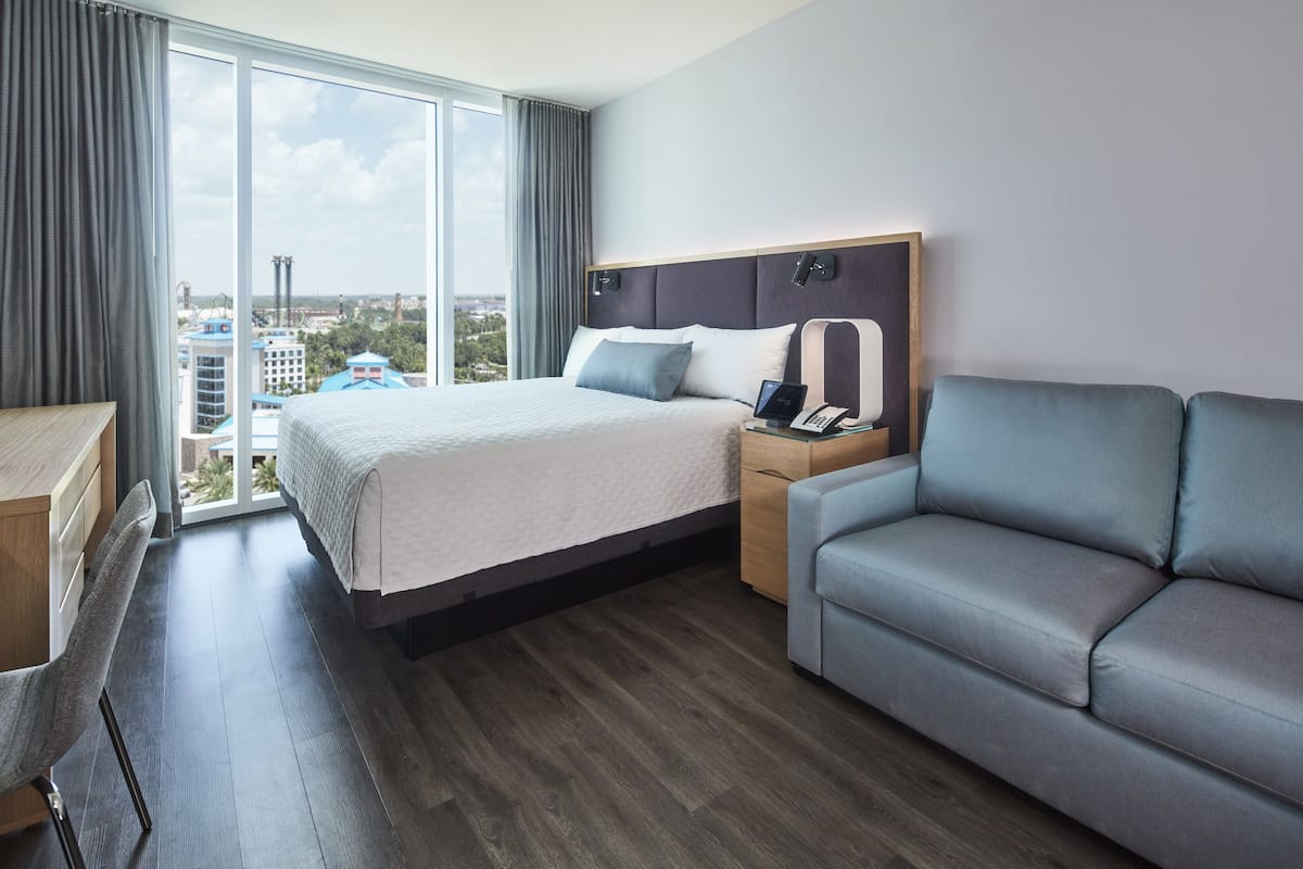 A hotel room with a large bed, a sofa, a desk, and a view of the city.