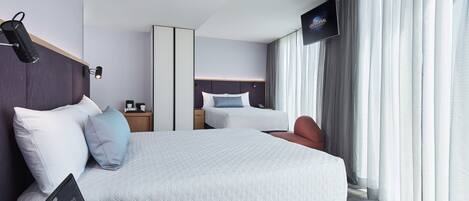 Ein modernes Hotelzimmer mit einem großen Bett, Nachttischen, einem Flachbildfernseher und Blick ins Freie durch große Fenster.