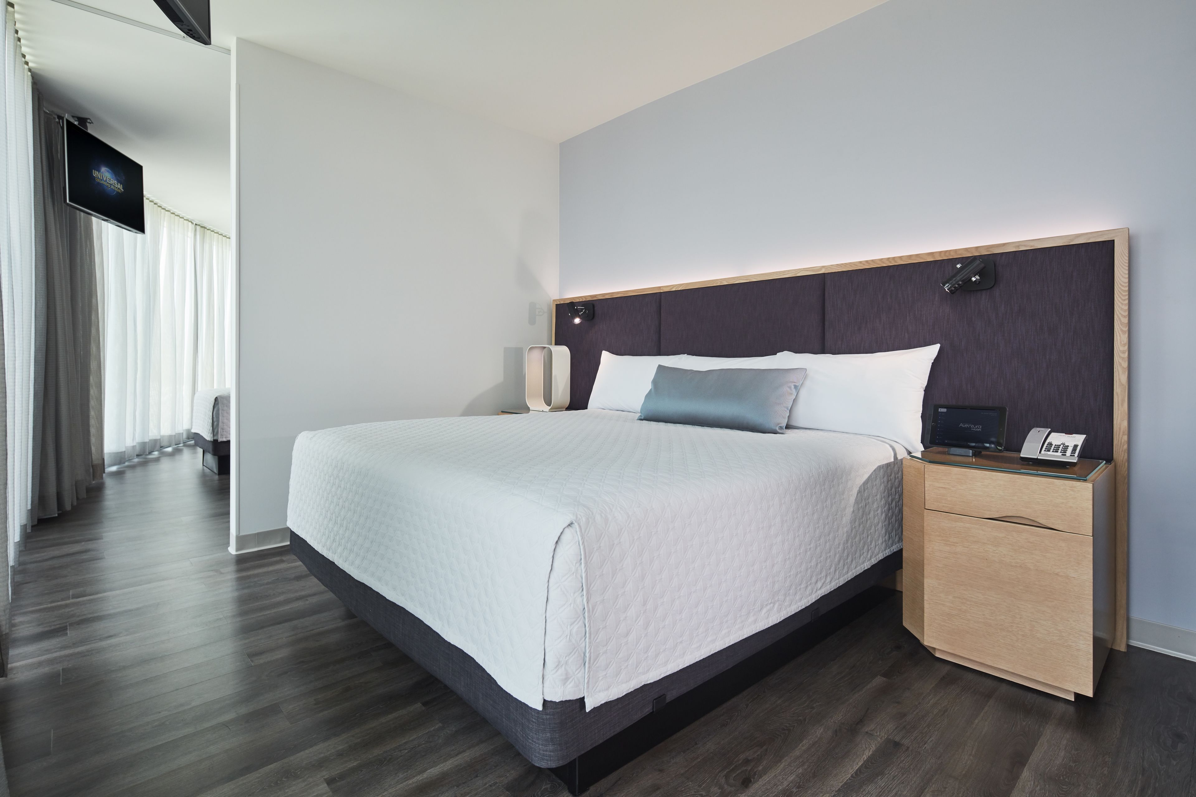 Een moderne hotelkamer met een groot bed, nachtkastjes, een flatscreen televisie en uitzicht op de gang.