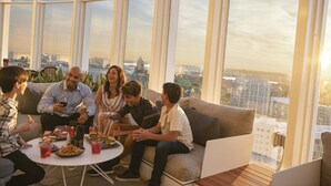 Un grupo de personas sentadas en un sofá y una mesa con comida y bebidas en una habitación con ventanas amplias.