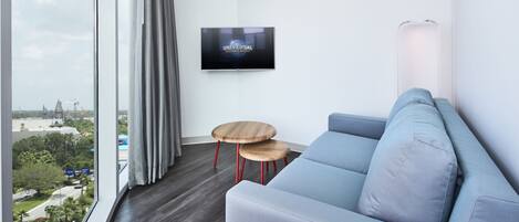 Uma sala de estar moderna com uma janela ampla, um sofá cinza, duas mesas laterais de madeira e uma TV de tela plana fixada na parede.