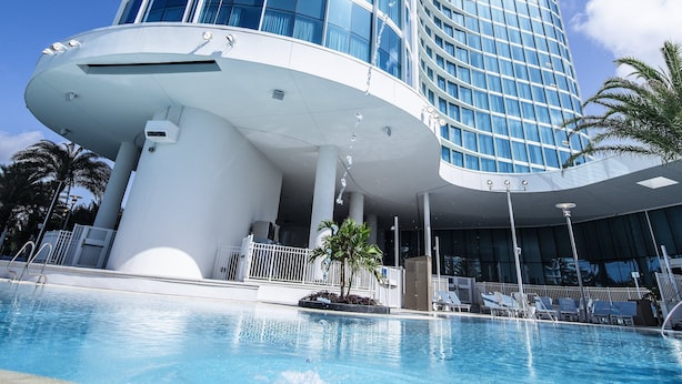 Un hotel moderno con fachada de vidrio curva, piscina y palmeras.