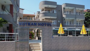 Exterior do Hotel Soykan, com entrada visível, entrada por portão e duas ombrelas amarelas.