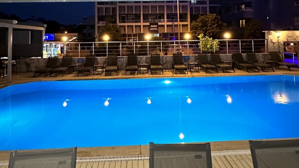 Piscina com espreguiçadeiras e um edifício ao fundo.