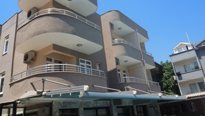 Edifício com várias andares, varandas, entrada coberta e câmera de segurança.