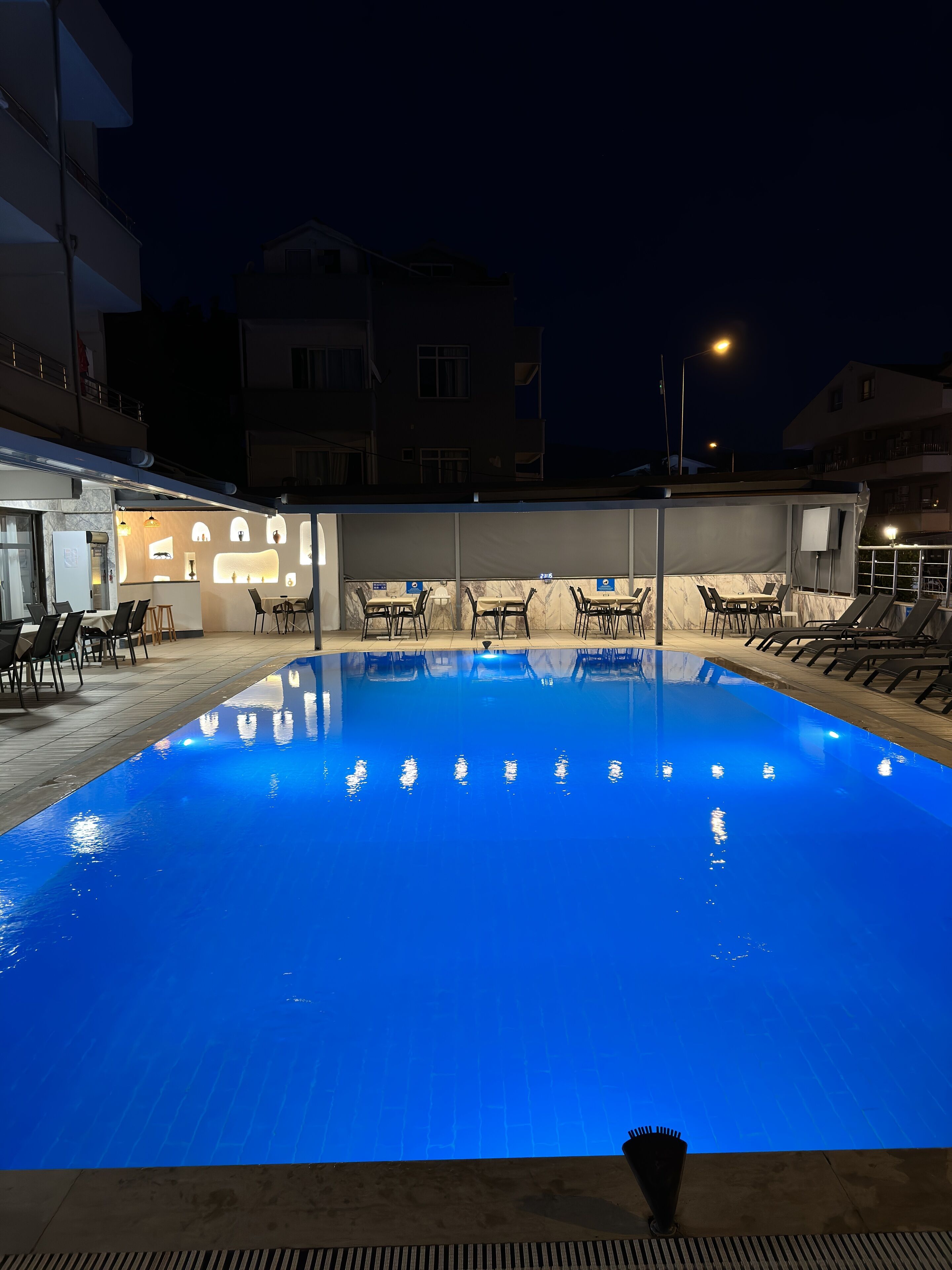 Una piscina con sillones de descanso y una zona de bar por la noche.