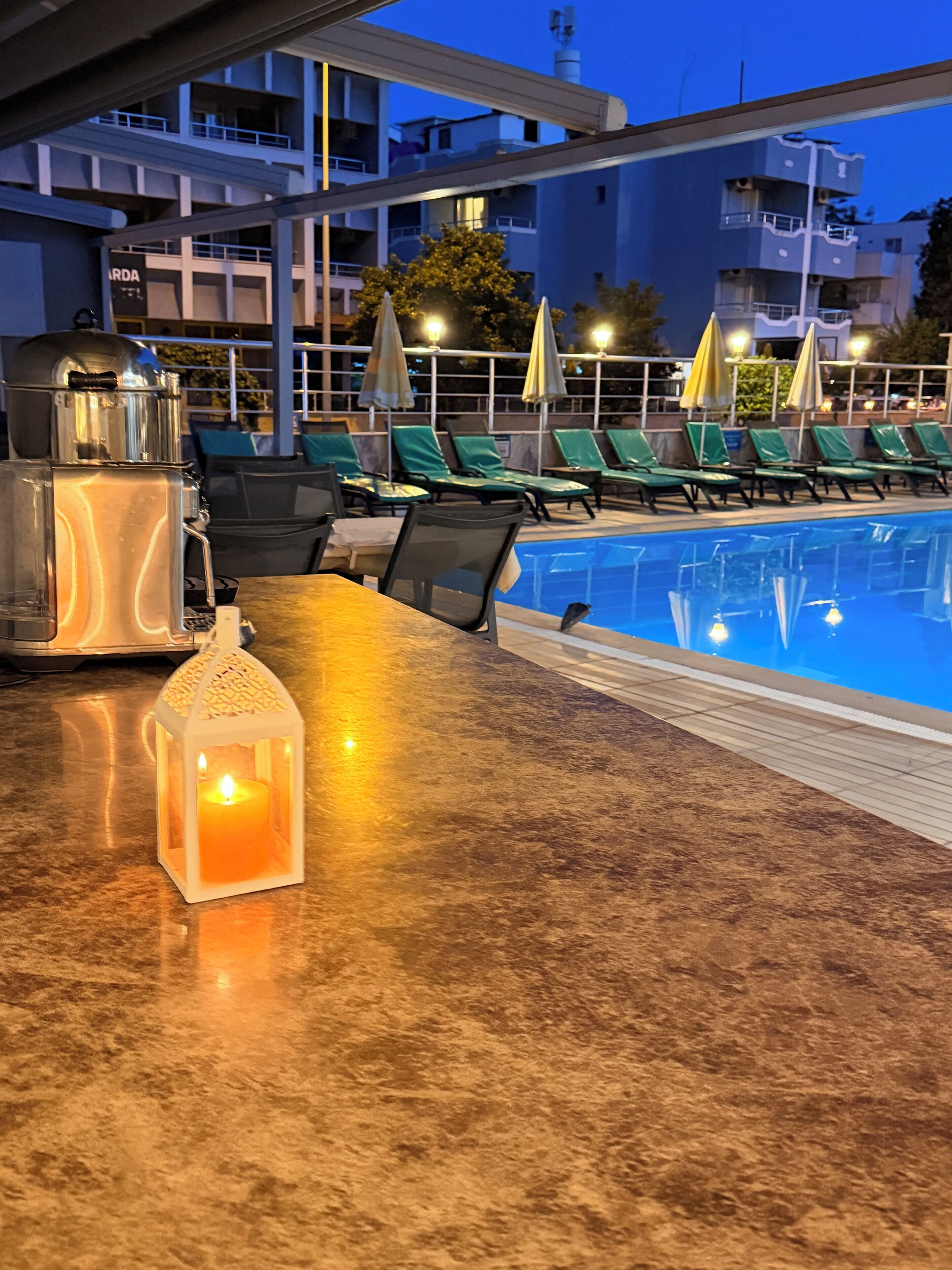 A poolside area with lounge chairs, a table with a water dispenser, and a candle lantern.