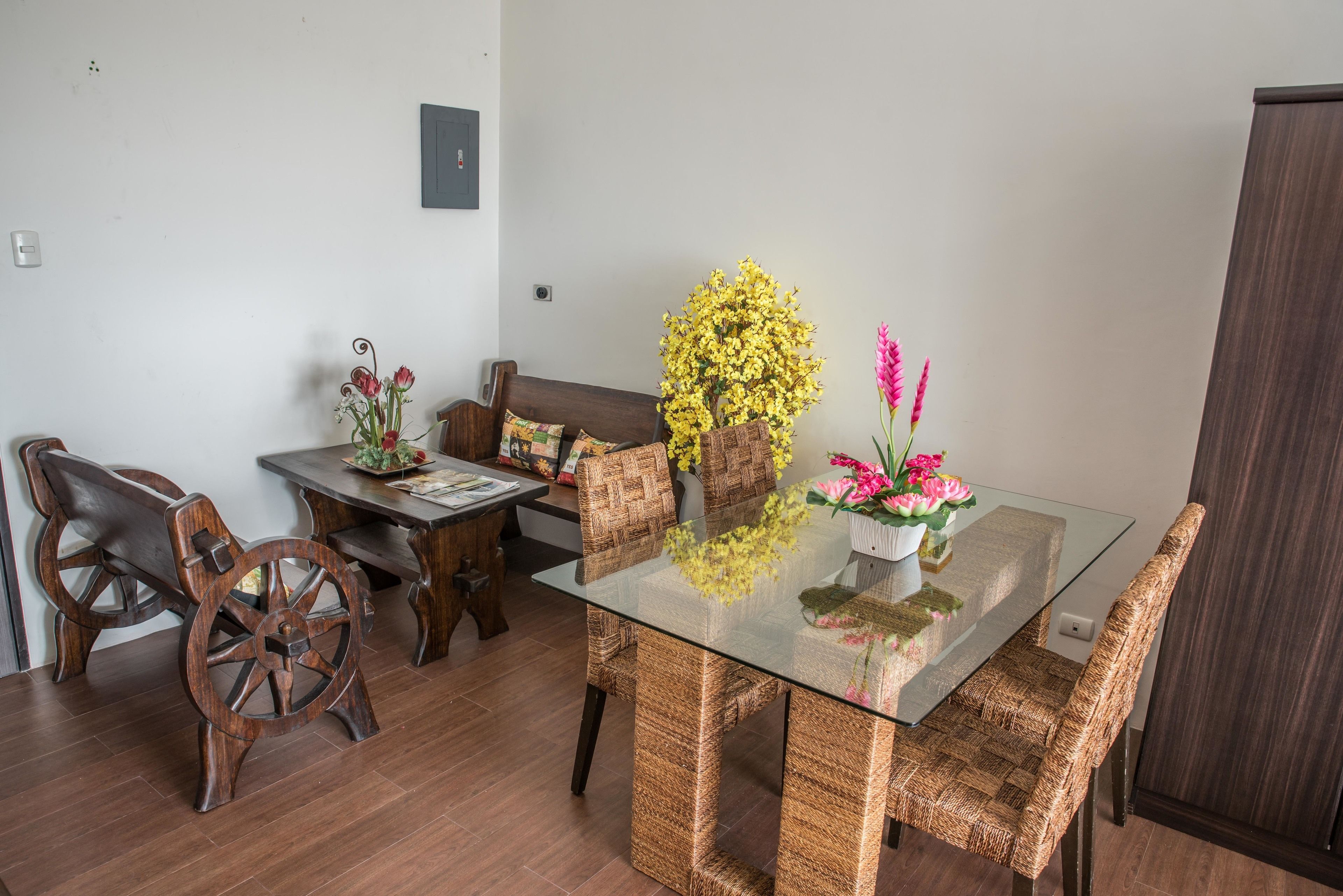 A dining area with a glass table, wicker chairs, a wooden bench, and a sofa.