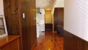 Un couloir avec un plancher en bois, un coin cuisine et un espace salon avec un canapé.