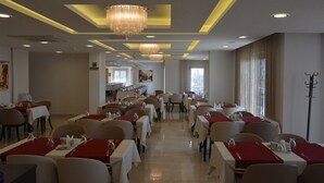Un comedor amplio con varias mesas, cada una con mantel blanco y camino de mesa rojo.
