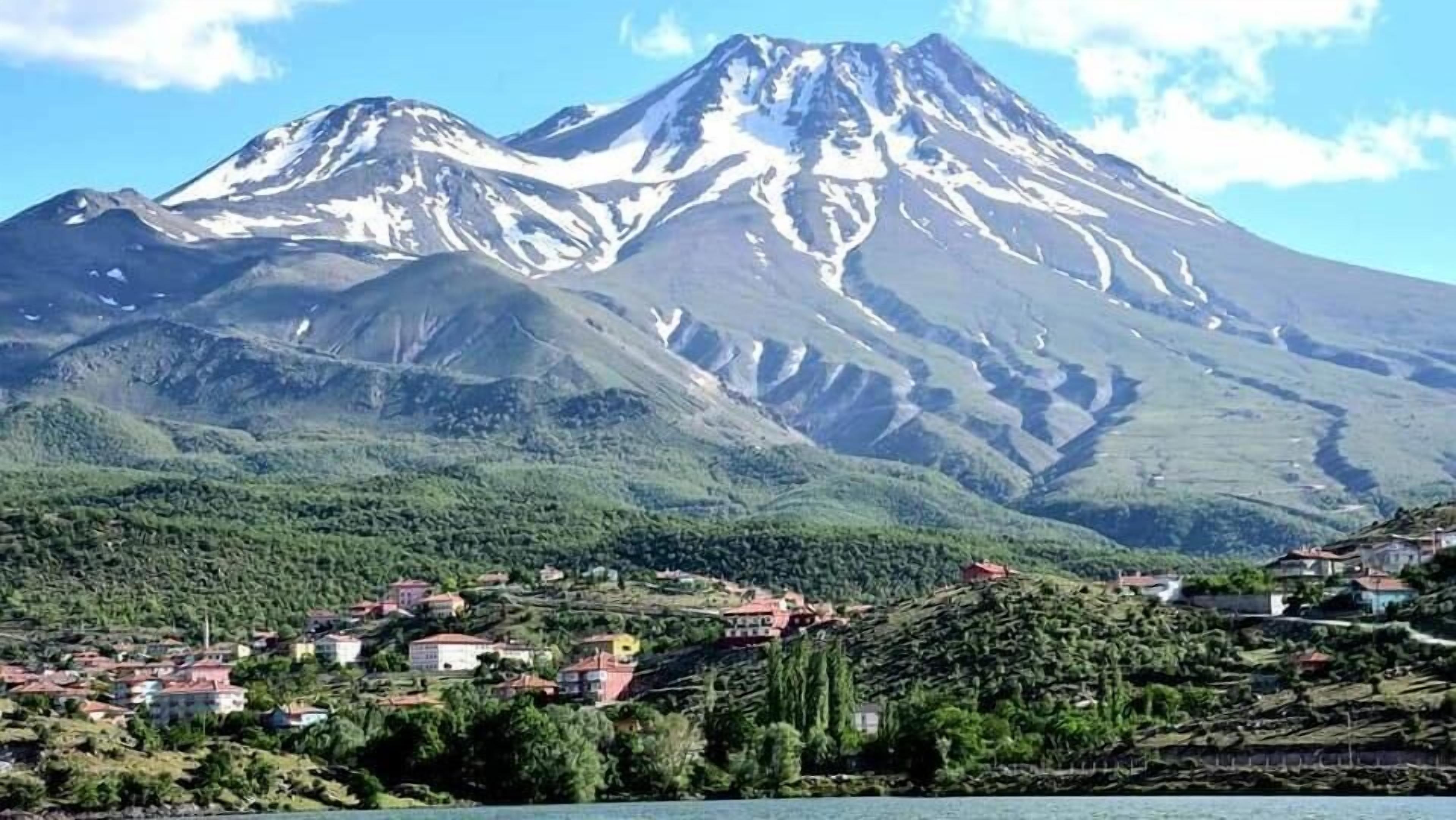 A mountain with snow-capped peaks and a town with red-roofed buildings at its base.