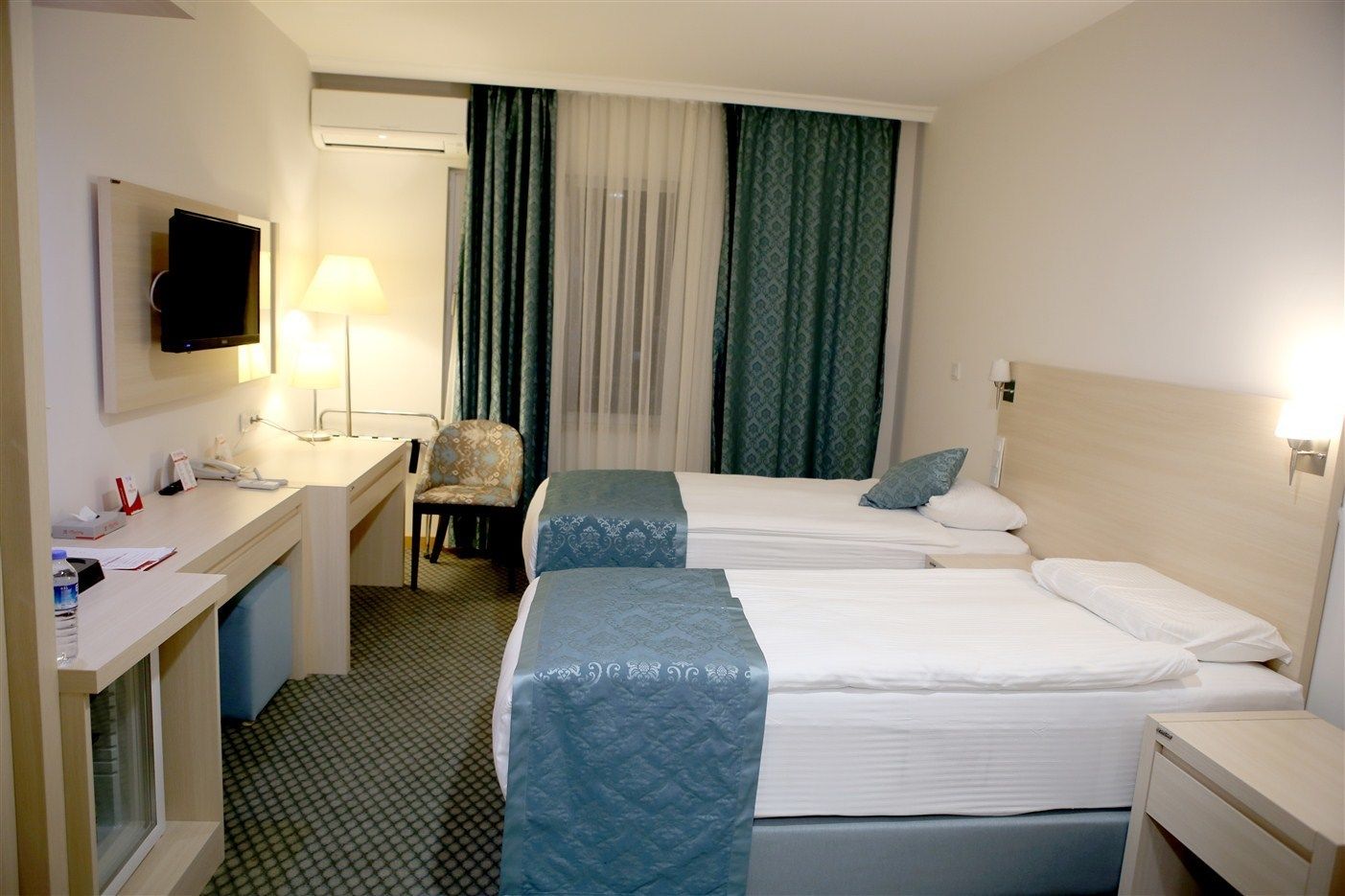 Habitación de hotel con dos camas, un escritorio, una silla, un televisor y una ventana con cortinas.