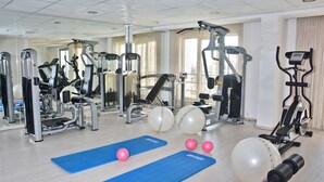 Un gimnasio con diversas máquinas de ejercicio, dos colchonetas azules y pelotas de fitness.