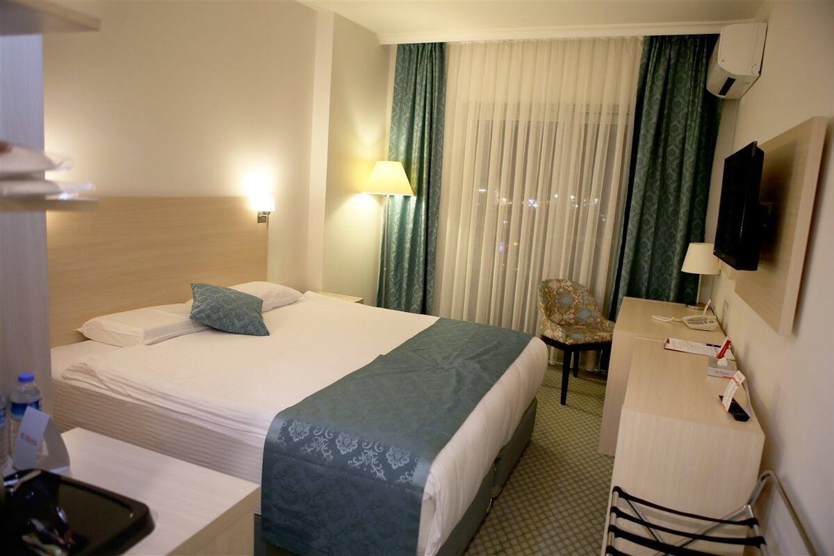 Habitación de hotel con cama, escritorio, silla, televisor y ventana con cortinas.