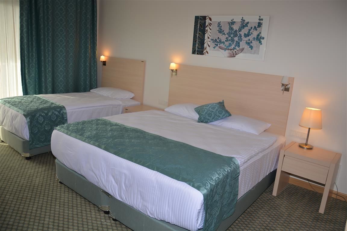Ein Hotelzimmer mit zwei Einzelbetten, jeweils mit grüner Bettdecke und weißen Laken. Zwei Nachttische mit Lampen stehen bereit, darüber befindet sich ein an der Wand befestigtes Kunstwerk.