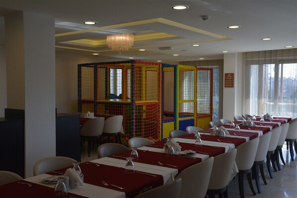 A restaurant with long tables, chairs, and a colorful play area for children.