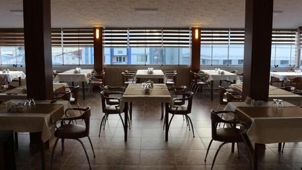 Un restaurante con varias mesas y sillas, amplias ventanas y vistas a edificios.
