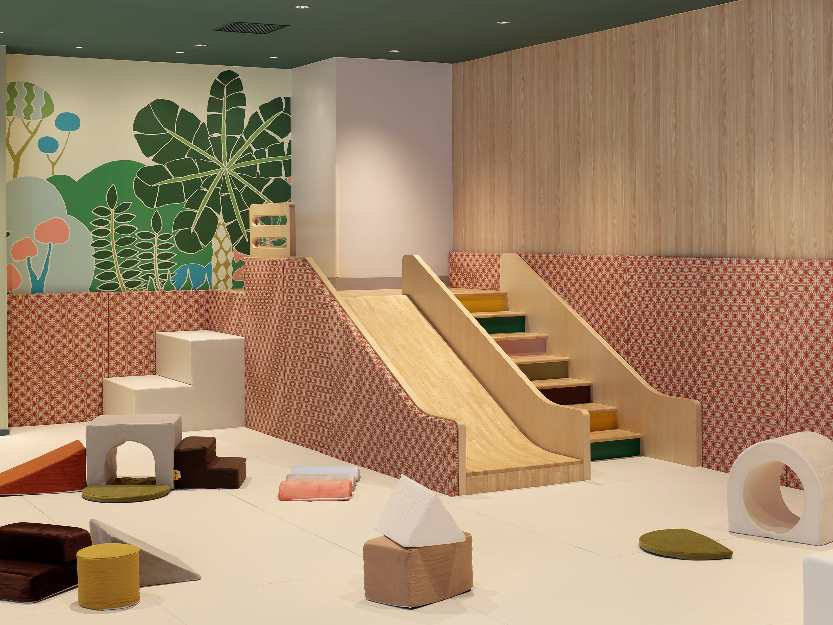 A playroom with a slide, soft play furniture, and a wall mural.