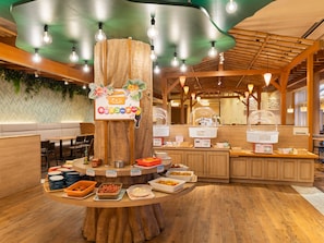 Un buffet disposé autour d’un tronc d’arbre en bois placé au centre, avec différents plats et un panneau indiquant l’emplacement du coin café.