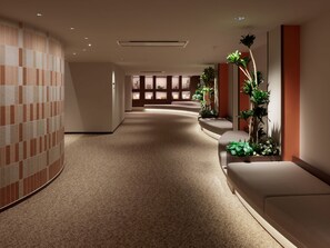 A hotel corridor with a curved wall, a seating area, and a plant arrangement. - Mitsui Garden Hotel Prana Tokyo Bay (Urayasu)